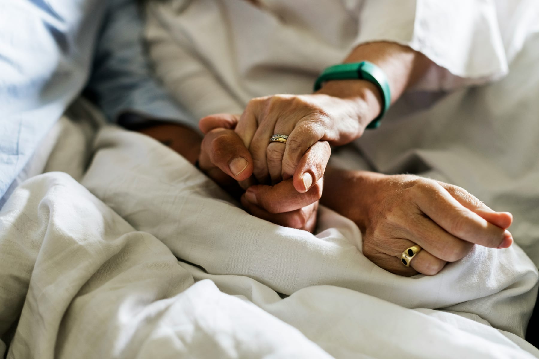 One person gently holding another person’s hand beside a bed
